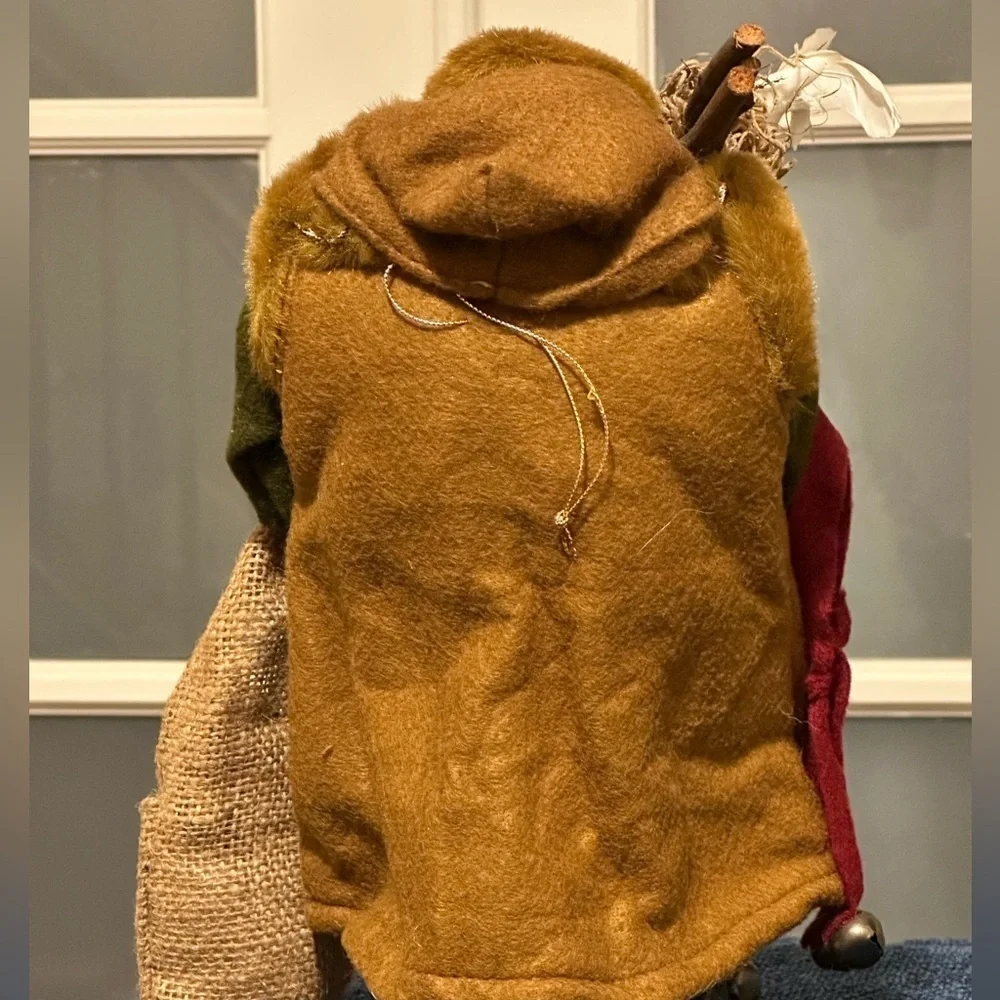 Shaggy haired and bearded Santa wears a brown cape and carries a burlap sack.